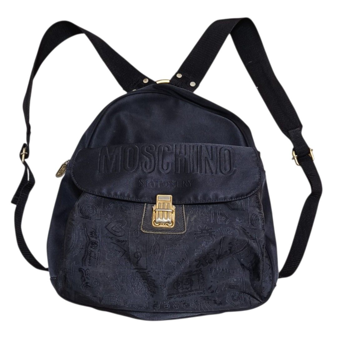 Cheap and Chic by Moschino Vintage Backpack (Category: Backpacks) located in Nasugbu. Submitted by staffpicks1515 (Listing ID 1468789890, Image 2). Description: - Brand: Cheap and Chic by Moschino - Material: Durable black canvas - Design: Embroidered Moschino lettering, gold-tone clasp, and subtle doodle pattern on the lower front - Features: Top zipper closure, adjustable fabric shoulder straps, and top carry ring - Interior: Includes signature