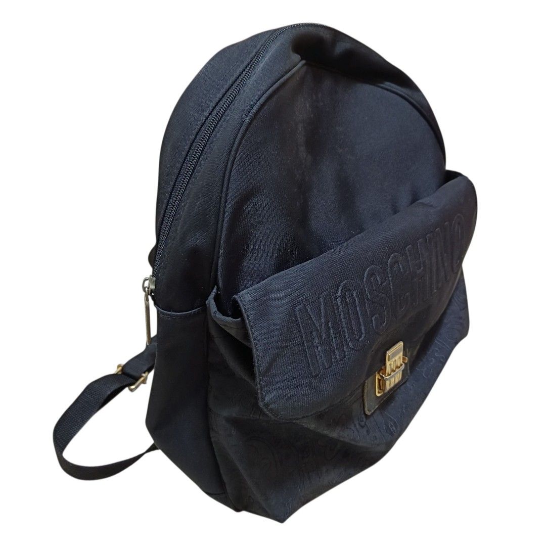 Cheap and Chic by Moschino Vintage Backpack (Category: Backpacks) located in Nasugbu. Submitted by staffpicks1515 (Listing ID 1468789890, Image 3). Description: - Brand: Cheap and Chic by Moschino - Material: Durable black canvas - Design: Embroidered Moschino lettering, gold-tone clasp, and subtle doodle pattern on the lower front - Features: Top zipper closure, adjustable fabric shoulder straps, and top carry ring - Interior: Includes signature
