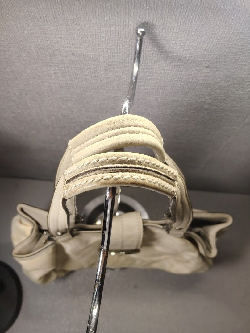 COACH CREAM SOHO LINEN (Category: Luxury Bags & Wallets) located in Valencia. Submitted by coolwolf_27a64f (Listing ID 1468739199, Image 3). Description: A vintage Coach Soho pleated linen and leather hobo bag displayed on a metal handbag stand. issue need clean no major flaws.