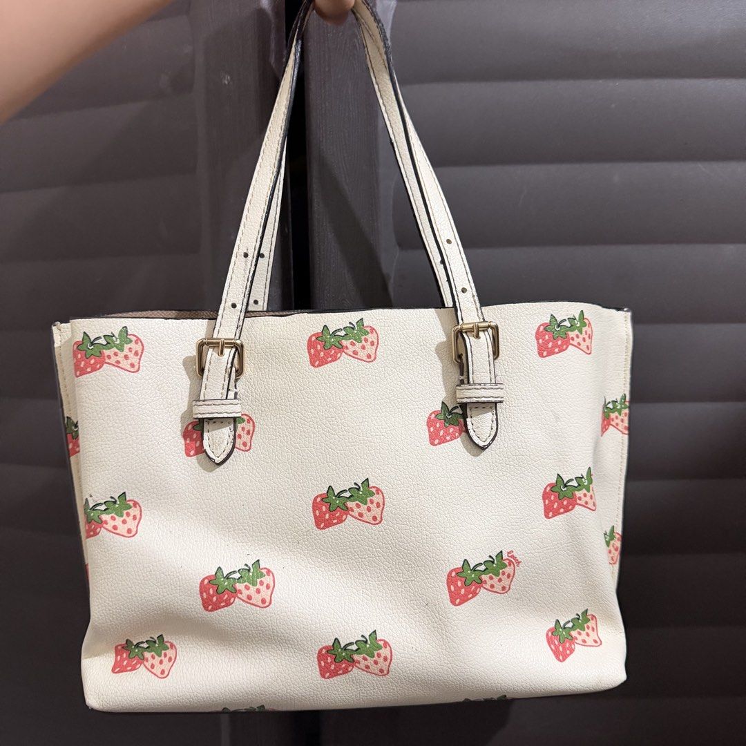 Coach Strawberry Print Tote Bag (Category: Tote Bags) located in Rizal. Submitted by lovegclothingph (Listing ID 1468858087, Image 2). Description: - Coach tote bag in white leather - Strawberry print pattern - Dual adjustable shoulder straps with buckle details - Includes signature gold-tone Coach hangtag - Vibrant pink fabric interior lining with creed patch - Flaw: Some peeling and wear visible along the edges of the handles - RFS: Declutterin