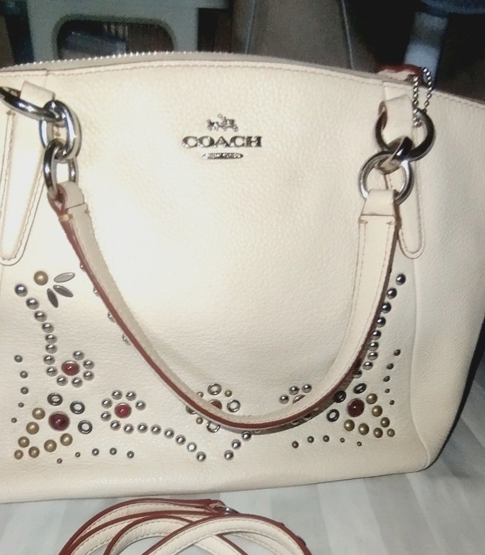 Coach White Leather Studded Satchel Bag with Strap (Category: Cross-body Bags) located in Manila. Submitted by lene48 (Listing ID 1468716837, Image 1). Description: - Brand: Coach - Style: Leather Satchel / Crossbody Bag - Color: Off-white with red and metallic front accents - Material: Premium pebble grain leather - Hardware: Silver-tone - Closure: Secure zippered top - Strap: Double top handles and a detachable shoulder strap - Condition: Clean
