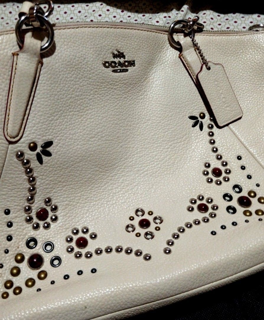 Coach White Leather Studded Satchel Bag with Strap (Category: Cross-body Bags) located in Manila. Submitted by lene48 (Listing ID 1468716837, Image 2). Description: - Brand: Coach - Style: Leather Satchel / Crossbody Bag - Color: Off-white with red and metallic front accents - Material: Premium pebble grain leather - Hardware: Silver-tone - Closure: Secure zippered top - Strap: Double top handles and a detachable shoulder strap - Condition: Clean