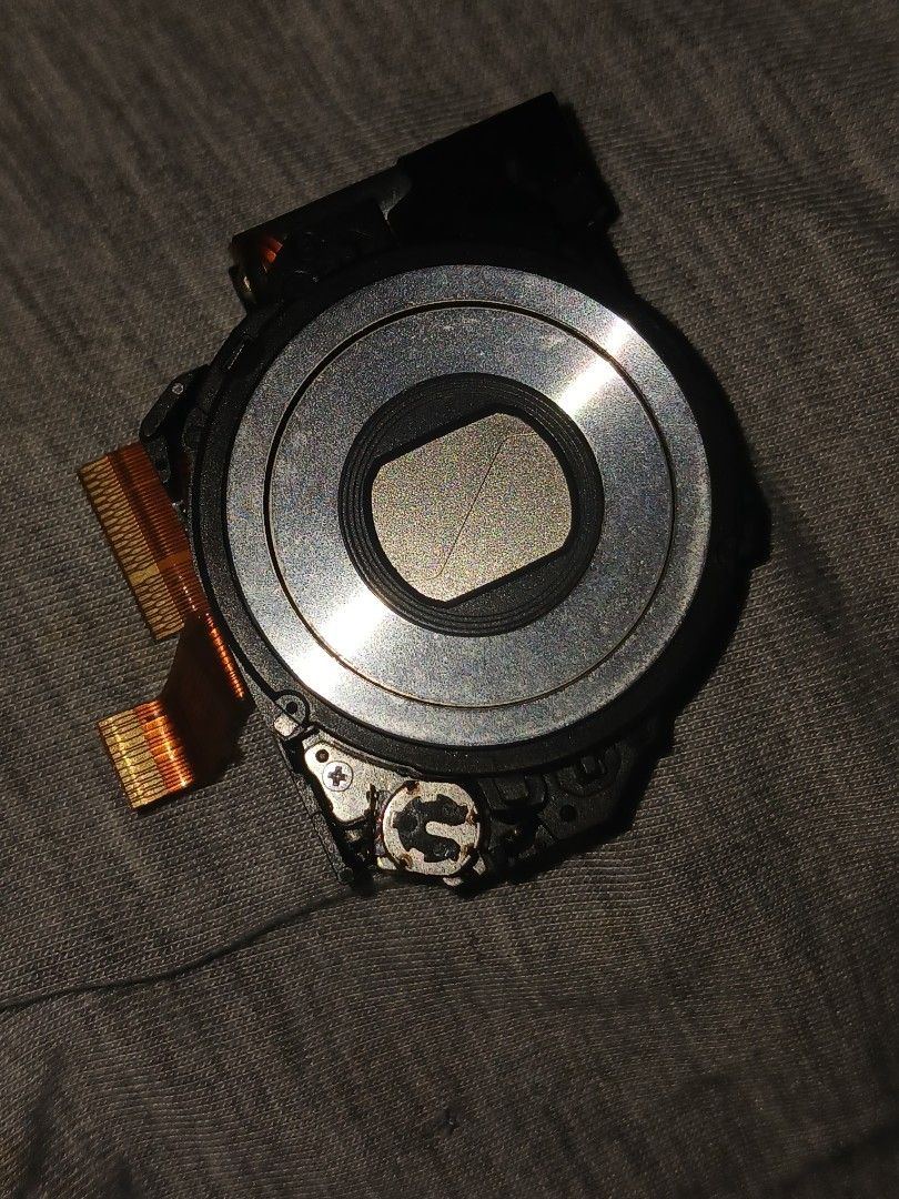 Compact Camera Lens Module Replacement Part (Category: Lens & Kits) located in Kalibo. Submitted by declutter.w.my (Listing ID 1468731894, Image 1). Description: - SONY CYBERSHOT W320 MODEL - Genuine camera lens module pulled from a dismantled digital camera - Includes flexible ribbon cables attached for easy integration - Features a round silver lens barrel with closed protective metal blades - Surrounded by a durable black plastic casing with a