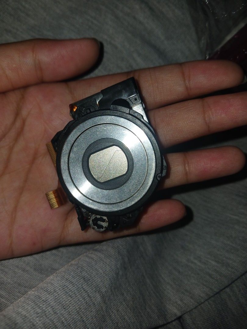Compact Camera Lens Module Replacement Part (Category: Lens & Kits) located in Kalibo. Submitted by declutter.w.my (Listing ID 1468731894, Image 2). Description: - SONY CYBERSHOT W320 MODEL - Genuine camera lens module pulled from a dismantled digital camera - Includes flexible ribbon cables attached for easy integration - Features a round silver lens barrel with closed protective metal blades - Surrounded by a durable black plastic casing with a