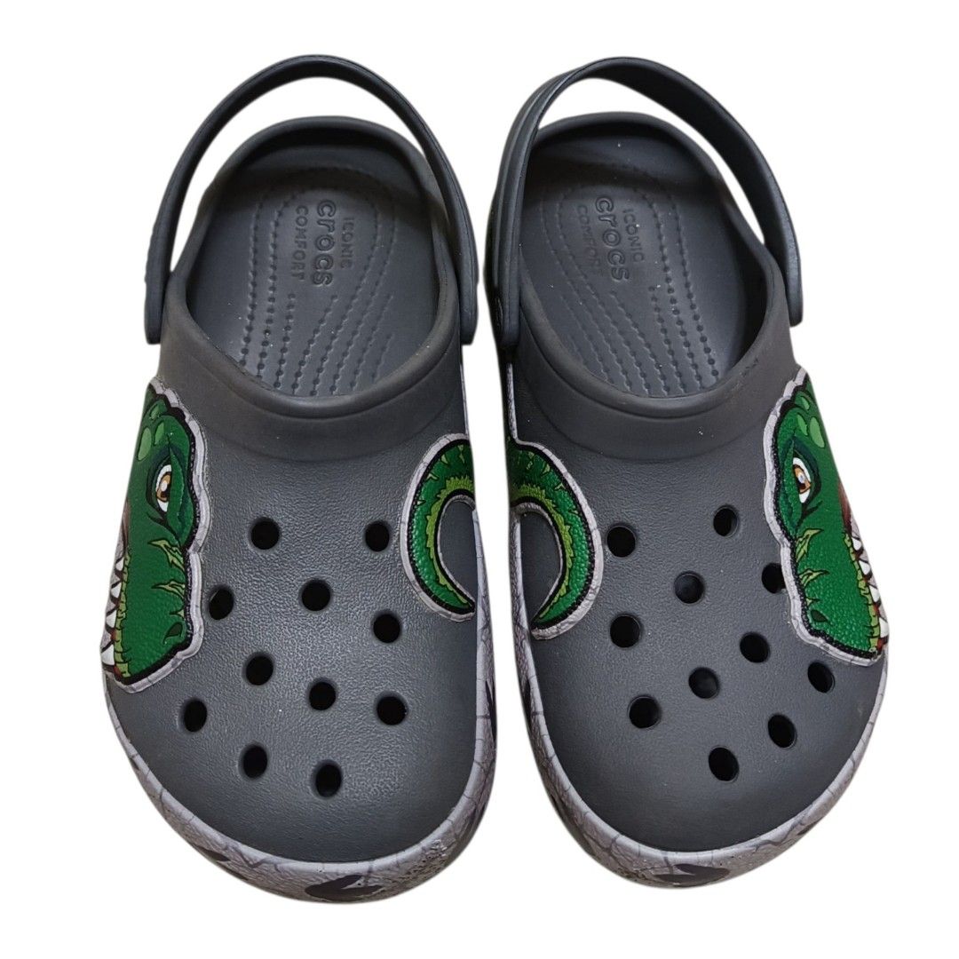 Crocs Kids Dinosaur Clog Size 13 (Category: Babies & Kids Fashion) located in Nasugbu. Submitted by staffpicks1515 (Listing ID 1468792044, Image 3). Description: - Size: Kids 13 - Color: Grey with green dinosaur graphic and tail wrap-around design - Features: Iconic Crocs comfort insoles, slip-on style, and secure back strap - Origin: Made in Vietnam - Condition: Normal signs of usage.