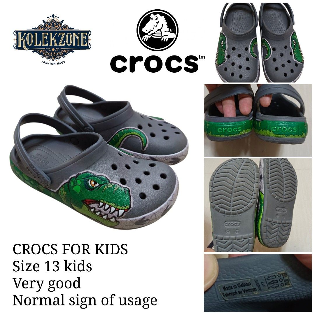 Crocs Kids Dinosaur Clog Size 13 (Category: Babies & Kids Fashion) located in Nasugbu. Submitted by staffpicks1515 (Listing ID 1468792044, Image 1). Description: - Size: Kids 13 - Color: Grey with green dinosaur graphic and tail wrap-around design - Features: Iconic Crocs comfort insoles, slip-on style, and secure back strap - Origin: Made in Vietnam - Condition: Normal signs of usage.