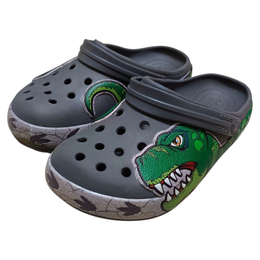 Crocs Kids Dinosaur Clog Size 13 (Category: Babies & Kids Fashion) located in Nasugbu. Submitted by staffpicks1515 (Listing ID 1468792044, Image 2). Description: - Size: Kids 13 - Color: Grey with green dinosaur graphic and tail wrap-around design - Features: Iconic Crocs comfort insoles, slip-on style, and secure back strap - Origin: Made in Vietnam - Condition: Normal signs of usage.