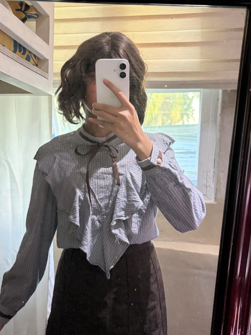 Dark Academia Ribbon Blouse (Category: Blouses) located in San Mateo. Submitted by heiayafinds (Listing ID 1468837445, Image 1). Description: A blue-gray pinstriped blouse featuring a dramatic layered ruffle front, a delicate brown ribbon bow at the neckline, a classic collarless round neckline, and long sleeves with buttoned cuffs. The cascading ruffles create a romantic vintage-inspired look, perfect for a soft coquette, dark academia, or vinta