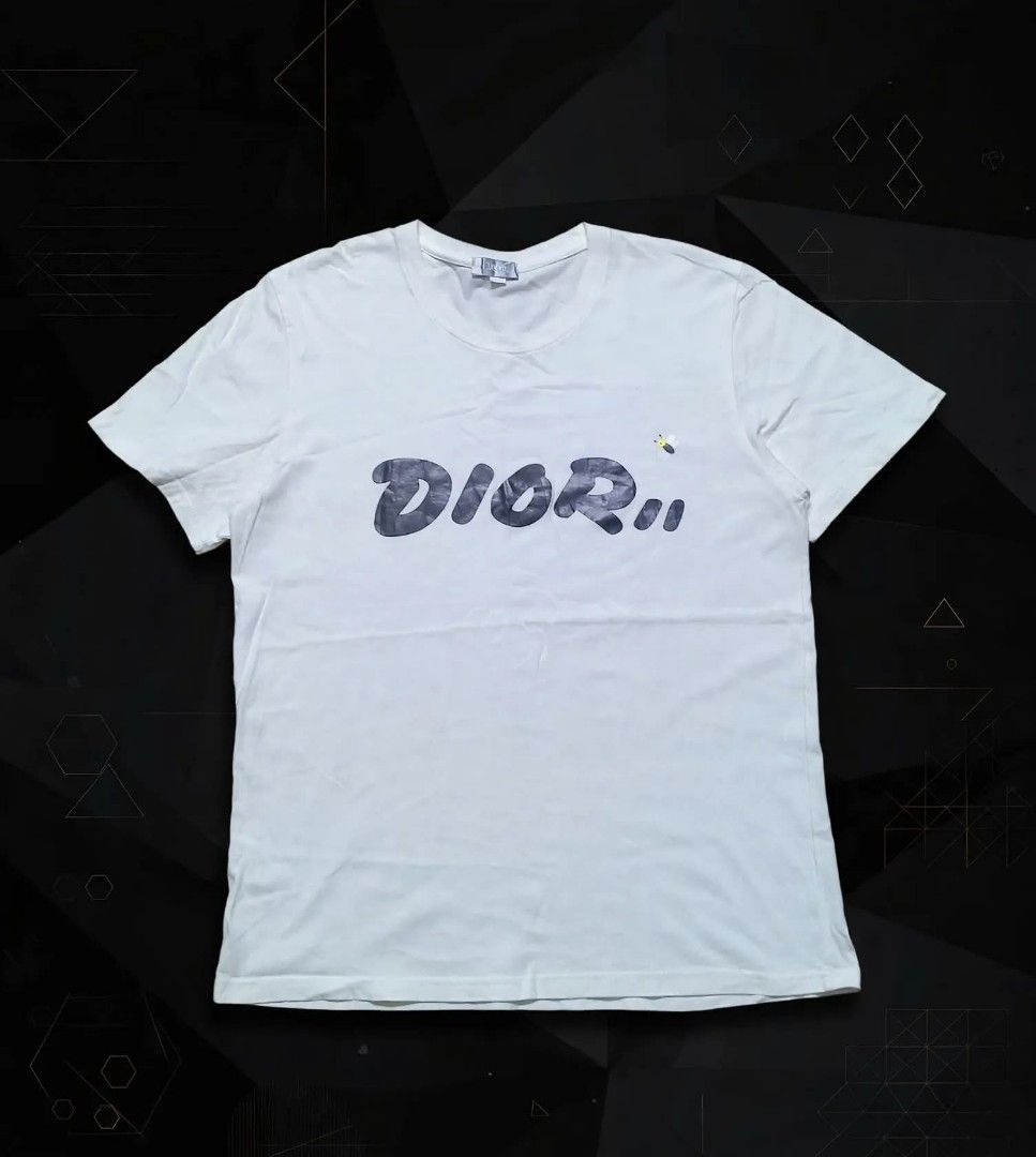 Dior Graffiti Bee White T-Shirt I Tee (Category: Tshirts & Polo Shirts ) located in Aguinaldo. Submitted by ukayandthrift (Listing ID 1468811930, Image 1). Description: - Brand: Dior - Color: Crisp white - Material: Premium cotton - Design: Graffiti-style lettering with signature embroidered bee graphic - Fit: Classic fit with crew neck and short sleeves - Condition: Clean fabric, collar tag intact.