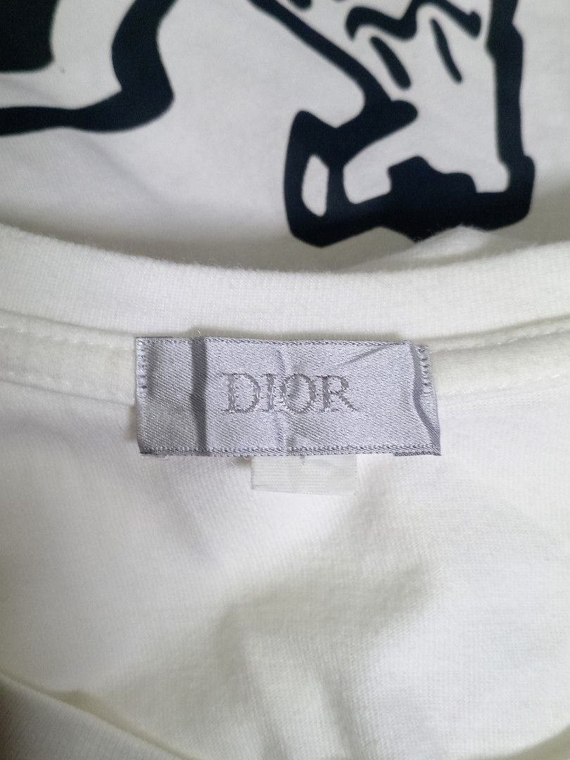 Dior Graffiti Bee White T-Shirt I Tee (Category: Tshirts & Polo Shirts ) located in Aguinaldo. Submitted by ukayandthrift (Listing ID 1468811930, Image 2). Description: - Brand: Dior - Color: Crisp white - Material: Premium cotton - Design: Graffiti-style lettering with signature embroidered bee graphic - Fit: Classic fit with crew neck and short sleeves - Condition: Clean fabric, collar tag intact.