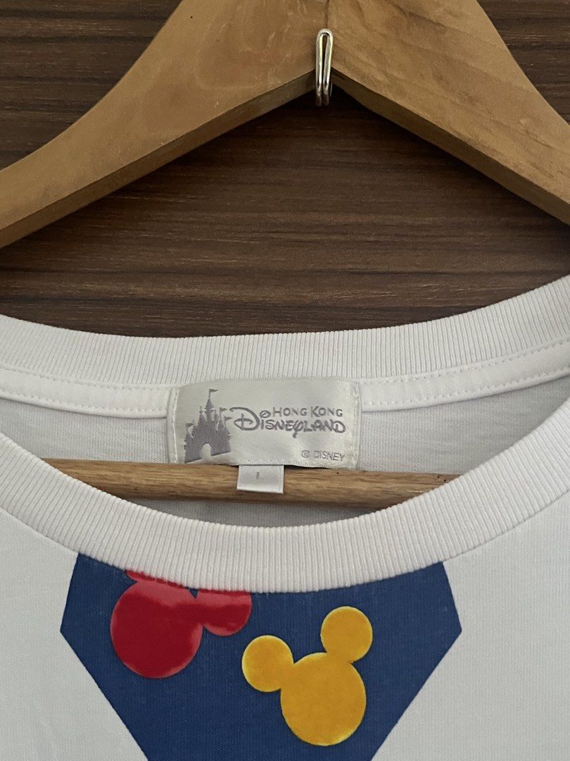 Disneyland Mickey Mouse Shirt (Category: Tshirts & Polo Shirts ) located in Manila. Submitted by thrifted.shits (Listing ID 1468766621, Image 2). Description: - Item: Hong Kong Disneyland Mickey Mouse Graphic Tee - Color: White - Size: L (Tag attached) - Design: Front features Mickey peeking behind a blue tie with red/yellow silhouettes; back features a large Mickey silhouette in striped shirt and blue shorts - Details: Short sleeves, crew neck -