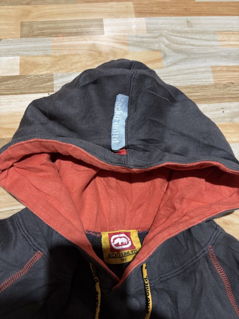 Ecko Unltd. Hooded Sweatshirt Grey Orange Size 140 (Category: Coats, Jackets and Outerwear) located in Tubigon. Submitted by wawiesunbe75372 (Listing ID 1468843365, Image 3). Description: - Brand: Ecko Unltd. - Size: 140 (Kids/Youth) - Color: Grey with vibrant orange accents and yellow drawstrings - Design: Large logo graphics on the chest and back hem - Features: Kangaroo pocket, contrast orange stitching throughout, and ribbed cuffs/hem - Condi