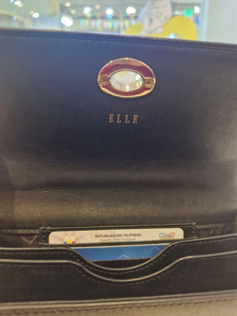ELLE Black Sling Wallet (Category: Cross-body Bags) located in Las Pinas. Submitted by jmproperties (Listing ID 1468798562, Image 3). Description: - Brand: ELLE - Color: Black with chic gold-tone hardware - Material: Textured leather finish - Versatile carry: Includes a top handle and removable shoulder strap - Interior: Divided compartments, fabric lining, and multiple card slots for easy organization - Condition: Clean inside and out with minim