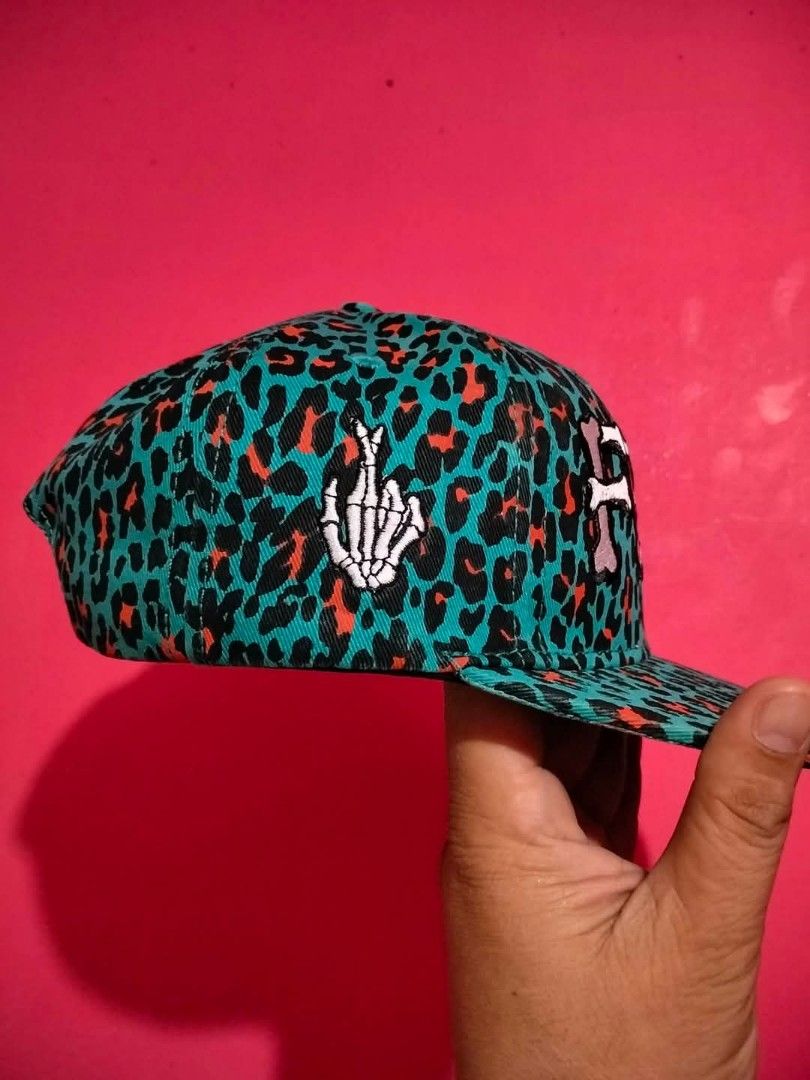 Fingercroxx Teal Leopard Print Snapback Cap (Category: Caps & Hats) located in Mangaldan. Submitted by niftythrifty69 (Listing ID 1468780988, Image 2). Description: - Brand: Fingercroxx - Style: Snapback hat with adjustable plastic snap closure - Design: Vibrant teal, black, and orange leopard print all over - Details: White embroidered bone-shaped FGXX logo on front and skeleton hand patch on the side - Interior: Features branded interior taping