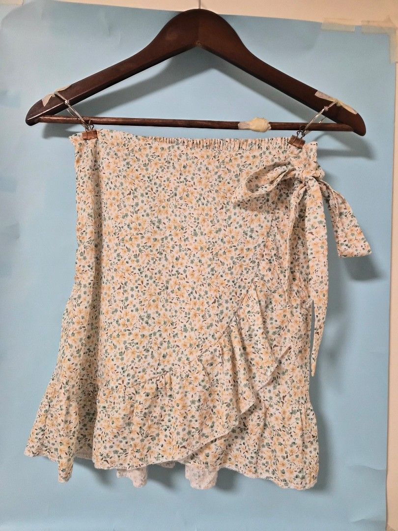 Floral Ruffle Wrap Skirt with Bow Tie (Category: Skirts) located in Manila. Submitted by prelovedbyc.hannah (Listing ID 1468771810, Image 2). Description: - Floral wrap skirt with white base and small yellow/green flowers - Features a sweet side tie ribbon and trendy ruffled hem - Comfortable fit with an elastic waistband at the back and side zipper - Comes with a white inner lining underneath for extra coverage - Made of light and flowy material