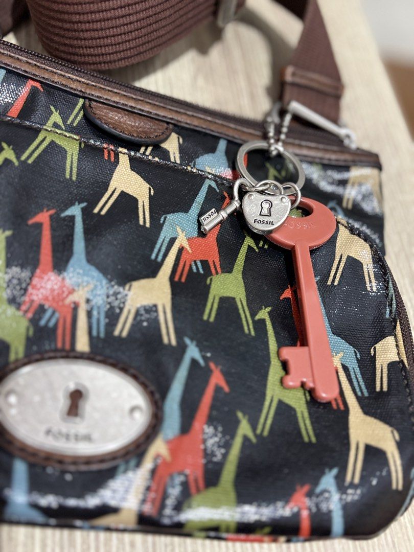 Fossil Giraffe Print Crossbody Bag with Key Charm (Category: Cross-body Bags) located in Makati City. Submitted by littlepinkpony (Listing ID 1468772000, Image 3). Description: Fossil crossbody bag featuring a colorful giraffe pattern printed on coated canvas. Brown fabric adjustable shoulder strap with silver-tone hardware. Front exterior zip pocket with the signature Fossil keyhole metal plaque. Includes hanging charm accents with a lock, small