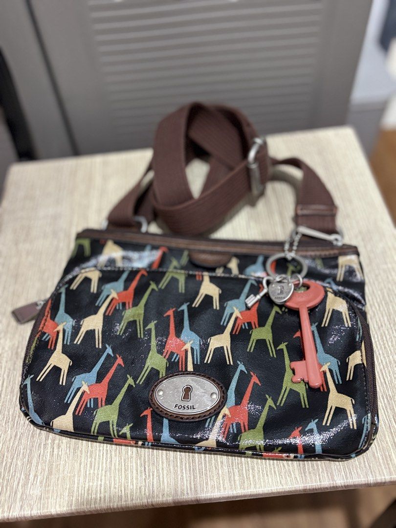 Fossil Giraffe Print Crossbody Bag with Key Charm (Category: Cross-body Bags) located in Makati City. Submitted by littlepinkpony (Listing ID 1468772000, Image 1). Description: Fossil crossbody bag featuring a colorful giraffe pattern printed on coated canvas. Brown fabric adjustable shoulder strap with silver-tone hardware. Front exterior zip pocket with the signature Fossil keyhole metal plaque. Includes hanging charm accents with a lock, small