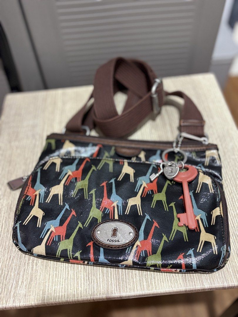 Fossil Giraffe Print Crossbody Bag with Key Charm (Category: Cross-body Bags) located in Makati City. Submitted by littlepinkpony (Listing ID 1468772000, Image 2). Description: Fossil crossbody bag featuring a colorful giraffe pattern printed on coated canvas. Brown fabric adjustable shoulder strap with silver-tone hardware. Front exterior zip pocket with the signature Fossil keyhole metal plaque. Includes hanging charm accents with a lock, small