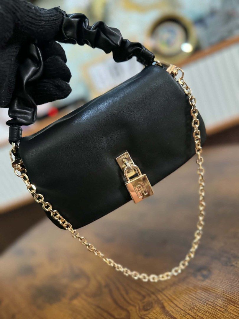 Furla Black Shoulder Bag with Chain Strap (Category: Luxury Bags & Wallets) located in Lipa City. Submitted by thyra06 (Listing ID 1468838515, Image 1). Description: - Color & Material: Premium black leather with sleek gold hardware - Handles: Unique ruched top handle and an adjustable chain strap - Closure: Secure lock closure on the front flap - Interior: Fabric-lined with a zip pocket and slip pockets for easy organization - Base: Clean textur