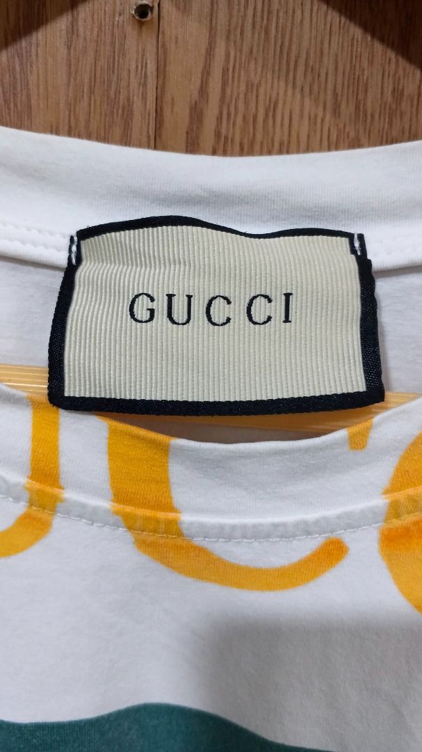 Gucci White T-Shirt Multi Logo Oversized (Category: Shirts) located in Oton. Submitted by offtherack.ilocity (Listing ID 1468739352, Image 2). Description: - Gucci white t-shirt - Size: Length 28; Width 22 Large to Xlarge - Features large interlocking GG logo with green and red stripe detail - Bold yellow and dark grey Gucci lettering stamped all around .