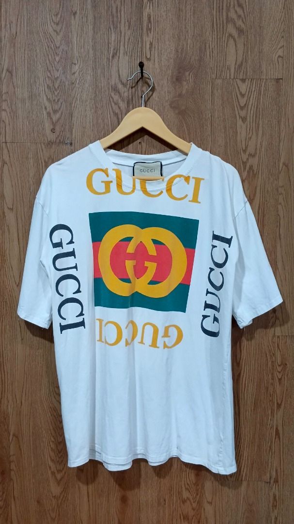 Gucci White T-Shirt Multi Logo Oversized (Category: Shirts) located in Oton. Submitted by offtherack.ilocity (Listing ID 1468739352, Image 1). Description: - Gucci white t-shirt - Size: Length 28; Width 22 Large to Xlarge - Features large interlocking GG logo with green and red stripe detail - Bold yellow and dark grey Gucci lettering stamped all around .