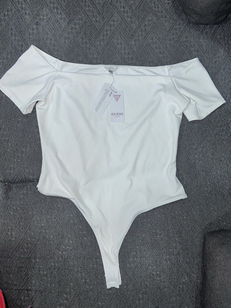 Guess Off-Shoulder White Bodysuit (Category: Blouses) located in Lubao. Submitted by ad_apparel (Listing ID 1468899289, Image 1). Description: - Brand: Guess - Style: Off-shoulder bodysuit with foldover neckline and short sleeves - Size: Large - Color: White - Details: Features a small silver Guess logo plaque and a thong bottom with snap closures - Condition: Brand new with original store tags still attached - Origin: Made in Vietnam.