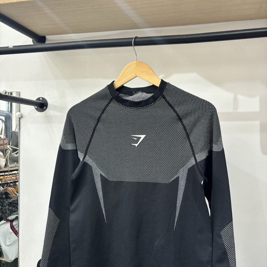 Gymshark Black Grey Long Sleeve Compression Shirt (Category: Activewear) located in Bambang. Submitted by heats777 (Listing ID 1468821994, Image 1). Description: - Brand: Gymshark - Color: Black and grey - Details: Mesh texture on chest, upper back, and sleeves - Branding: White Gymshark logo on chest and 'BEAVISIONARY' print on the inside elastic hem - Condition: Slight loose thread on the inner collar binding, otherwise great.