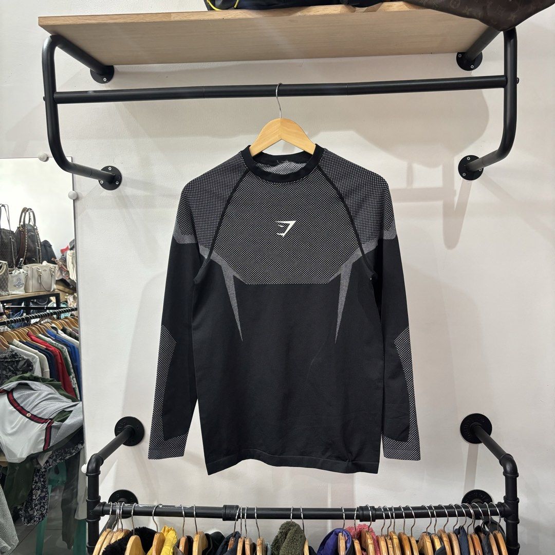 Gymshark Black Grey Long Sleeve Compression Shirt (Category: Activewear) located in Bambang. Submitted by heats777 (Listing ID 1468821994, Image 2). Description: - Brand: Gymshark - Color: Black and grey - Details: Mesh texture on chest, upper back, and sleeves - Branding: White Gymshark logo on chest and 'BEAVISIONARY' print on the inside elastic hem - Condition: Slight loose thread on the inner collar binding, otherwise great.