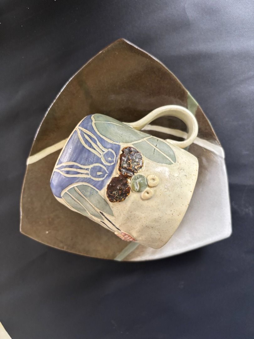 Handmade Ceramic Mug and Triangular Saucer Set (Category: Coffee & Tea Tableware) located in Baao. Submitted by apr1979 (Listing ID 1468785005, Image 3). Description: - Cup: 3.1 x 3.7 inches Triangle Footed Saucer/Trinket: 8 x 1.1 inches - Handmade ceramic mug with a cute raised frog face and plant designs - Glazed in charming beige, blue, and green tones - Comes with a unique triangular saucer featuring earthy brown and grey glazes with painted 