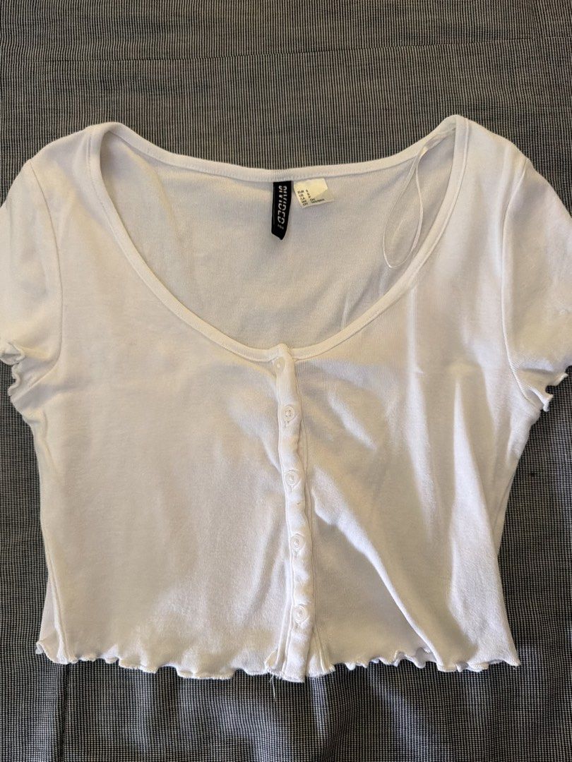 H&M Divided White Button Front Crop Top Size S (Category: Shirts) located in Manila. Submitted by jaehyun2829 (Listing ID 1468777085, Image 2). Description: - Brand: H&M Divided - Size: S (EUR S, US S) - Color: White - Material: Stretchy ribbed knit fabric - Design: Scoop neckline, short sleeves with lettuce hem, and front button placket - Condition: Great basic piece, perfect for layering or wearing with high-waisted denim.