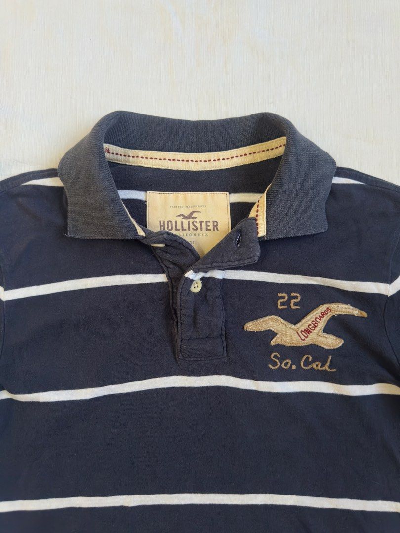 HOLLISTER (Category: Tshirts & Polo Shirts ) located in Davao. Submitted by kelsocool (Listing ID 1468802108, Image 2). Description: Hollister Navy Striped So.Cal Polo Shirt Size: S Dimes (inch): 27 - length 19 - width 8 - sleeve color rate: 8/10 good condition issue - minimal hole Description: Y2K-style Hollister navy blue horizontal striped polo featuring gold embroidered “So.Cal 22” seagull crest graphic..