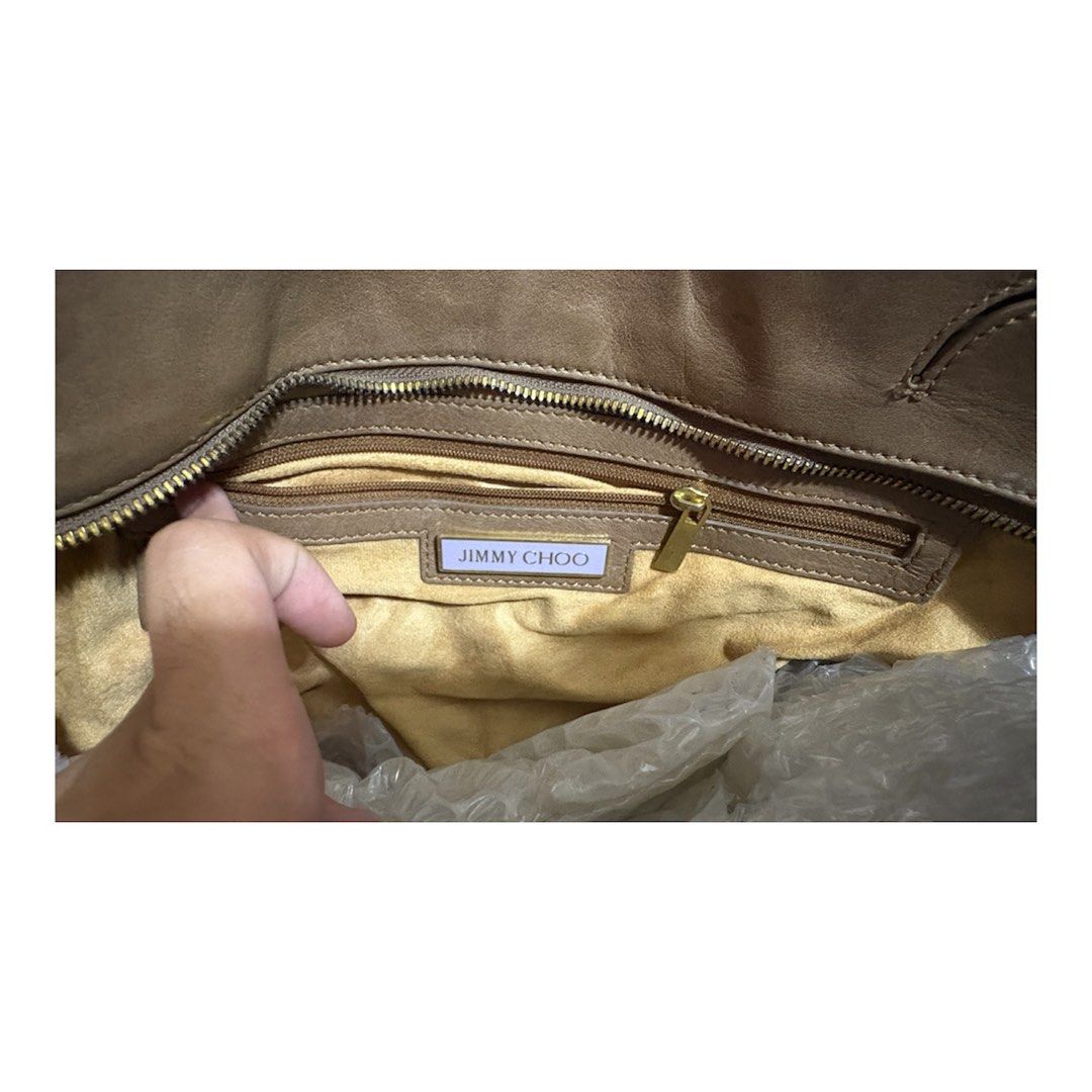 Jimmy Choo Taupe Leather Shoulder Bag (Category: Luxury Bags & Wallets) located in Los Banos. Submitted by amadea_c (Listing ID 1468752821, Image 3). Description: - Brand: Jimmy Choo - Material: Premium taupe leather - Hardware: Gold-tone with engraved logo plate - Closure: Center buckle strap - Strap: Black and gold-tone chain link - Interior: Fabric-lined with zippered pocket and brand plaque - Design: Spacious, slouchy everyday shoulder bag FO