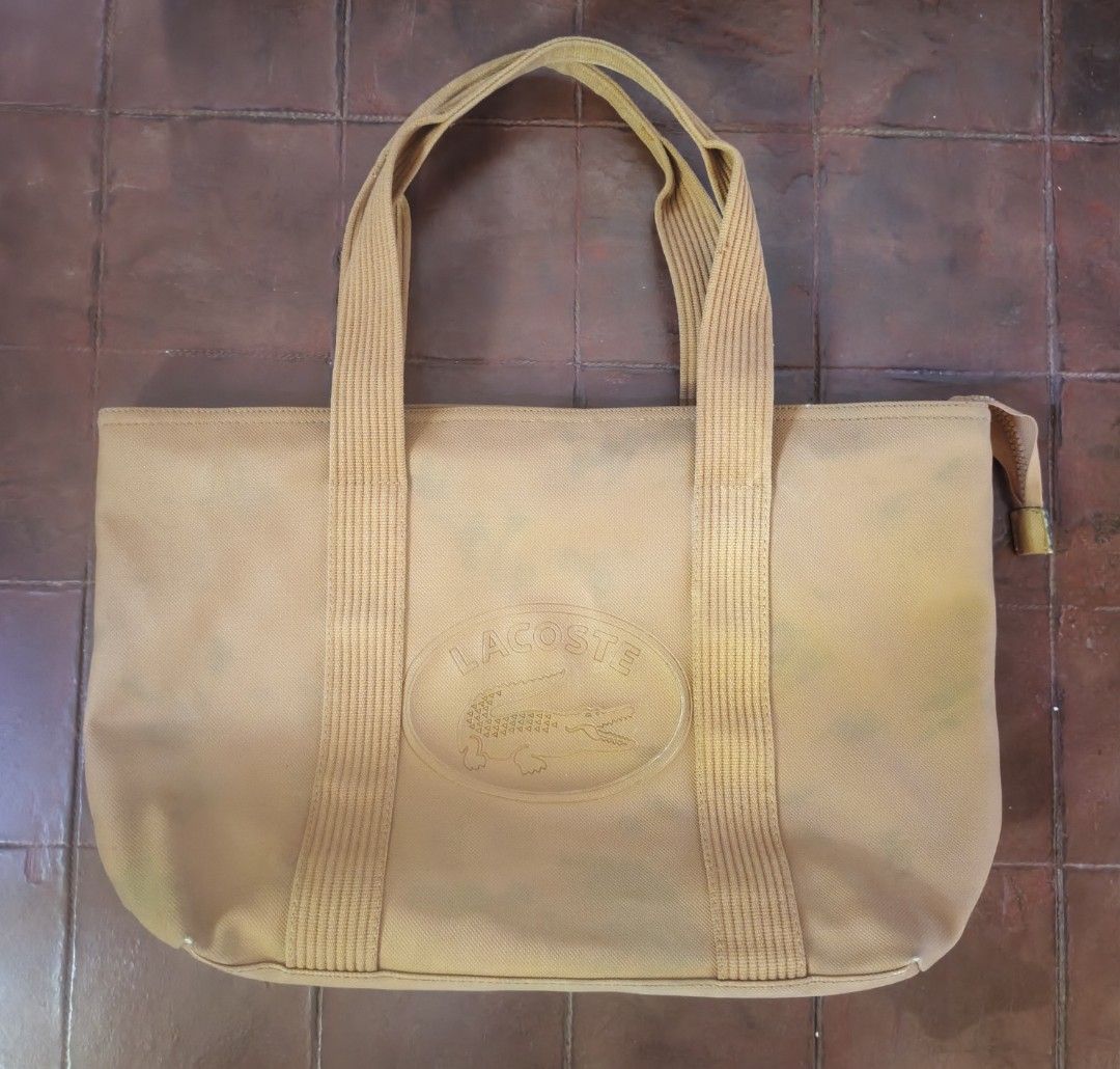Lacoste Yellow Canvas Tote Bag (Category: Tote Bags) located in Barobo. Submitted by edmarvall17 (Listing ID 1468740489, Image 1). Description: - Brand: Lacoste - Style: Tote bag in vibrant yellow with double shoulder straps - Exterior: Large embossed Lacoste logo patch on the front - Closure: Secure top zip closure - Interior: Tan lining with multiple fabric compartments and zippered pockets - Details: Tag indicates made in China with care instr