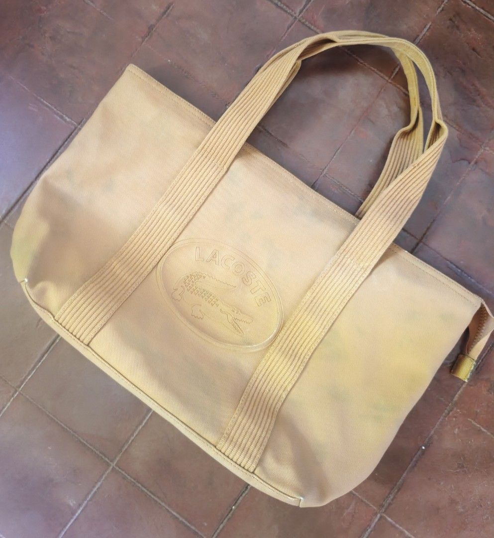 Lacoste Yellow Canvas Tote Bag (Category: Tote Bags) located in Barobo. Submitted by edmarvall17 (Listing ID 1468740489, Image 2). Description: - Brand: Lacoste - Style: Tote bag in vibrant yellow with double shoulder straps - Exterior: Large embossed Lacoste logo patch on the front - Closure: Secure top zip closure - Interior: Tan lining with multiple fabric compartments and zippered pockets - Details: Tag indicates made in China with care instr