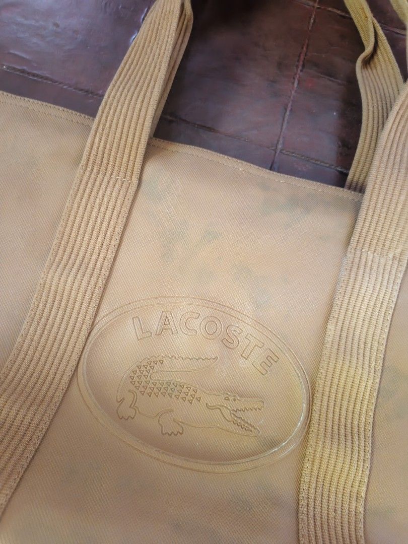 Lacoste Yellow Canvas Tote Bag (Category: Tote Bags) located in Barobo. Submitted by edmarvall17 (Listing ID 1468740489, Image 3). Description: - Brand: Lacoste - Style: Tote bag in vibrant yellow with double shoulder straps - Exterior: Large embossed Lacoste logo patch on the front - Closure: Secure top zip closure - Interior: Tan lining with multiple fabric compartments and zippered pockets - Details: Tag indicates made in China with care instr
