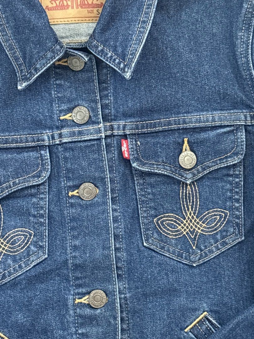Levi's Denim Jacket Size S (Category: Coats, Jackets and Outerwear) located in Manila. Submitted by ysballsz (Listing ID 1468809290, Image 3). Description: - Brand: Levi's - Style: Classic denim jacket with dark blue wash - Size: S (fits true to standard sizing) - Details: Button-up front, metallic hardware, classic collar - Pockets: Dual chest pockets with button closures and intricate contrast embroidery - Branding: Iconic red Levi's tab on the
