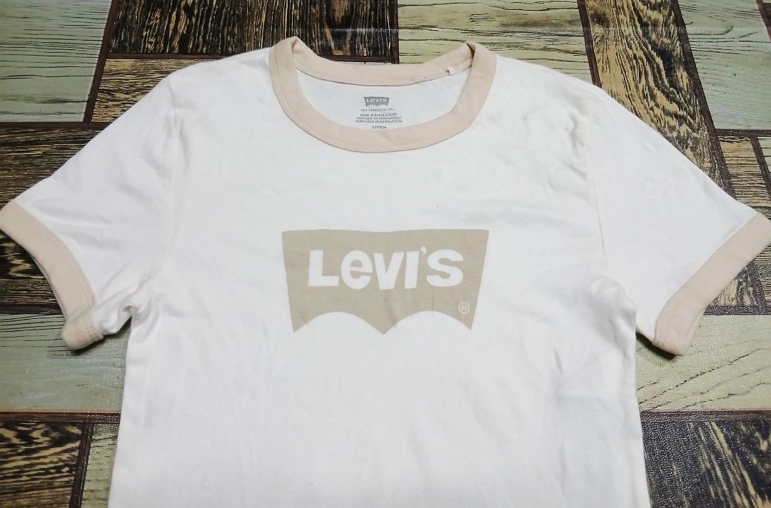 Levi's White Ringer T-Shirt Size S (Category: Shirts) located in Caloocan City. Submitted by youngmoon_51e2c6 (Listing ID 1468793408, Image 2). Description: - Brand: Levi's - Style: Ringer t-shirt with crew neck and short sleeves - Color: White with beige contrast trim on collar and cuffs - Graphic: Large Levi's batwing logo on front center - Size: S (155/80A) - Material: Soft cotton - Origin: Made in Bangladesh - Condition: Excellent / Tag detai
