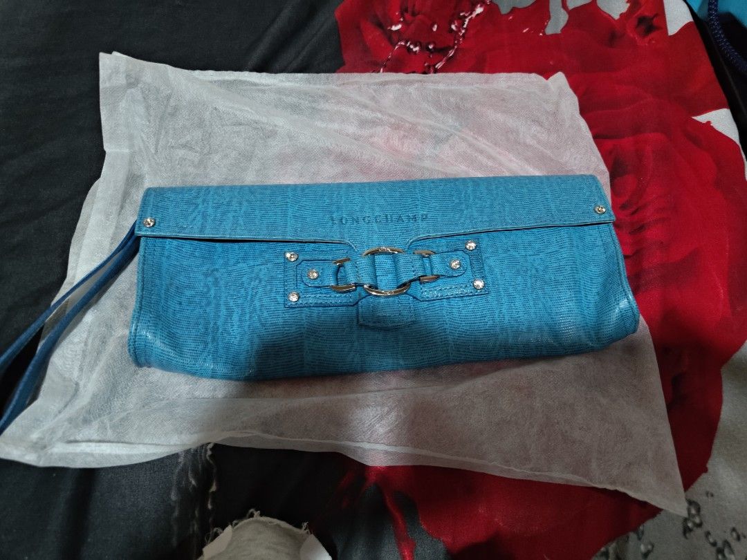 Longchamp Blue Lizard Texture Clutch Bag with Wrist Strap (Category: Luxury Bags & Wallets) located in Valenzuela. Submitted by wisewhale_46982b (Listing ID 1468779832, Image 1). Description: - Brand: Longchamp - Color: Bright blue with a chic lizard-texture finish - Hardware: Silver-tone decorative buckle, ring details, and sparkling rhinestone studs - Convenience: Matching blue wrist strap attached on the side - Interior: Signature blue branded