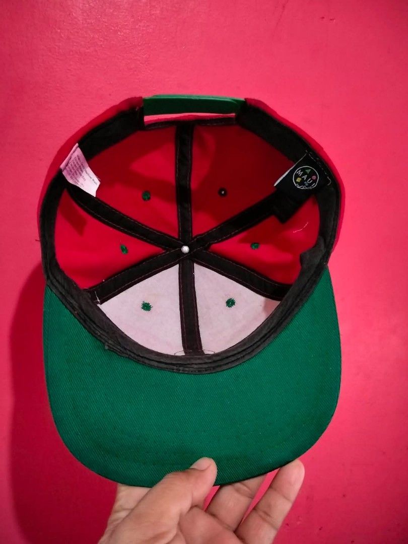 Maui and Sons Snapback Hat Red Green (Category: Caps & Hats) located in Mangaldan. Submitted by niftythrifty69 (Listing ID 1468734375, Image 3). Description: - Brand: Maui and Sons - Design: Round embroidered patch logo with colorful geometric shapes on the front - Colors: Vibrant red body with a contrast green flat brim - Fit: Adjustable snapback closure for a customized fit - Details: Interior features branded black taping and official tags - C