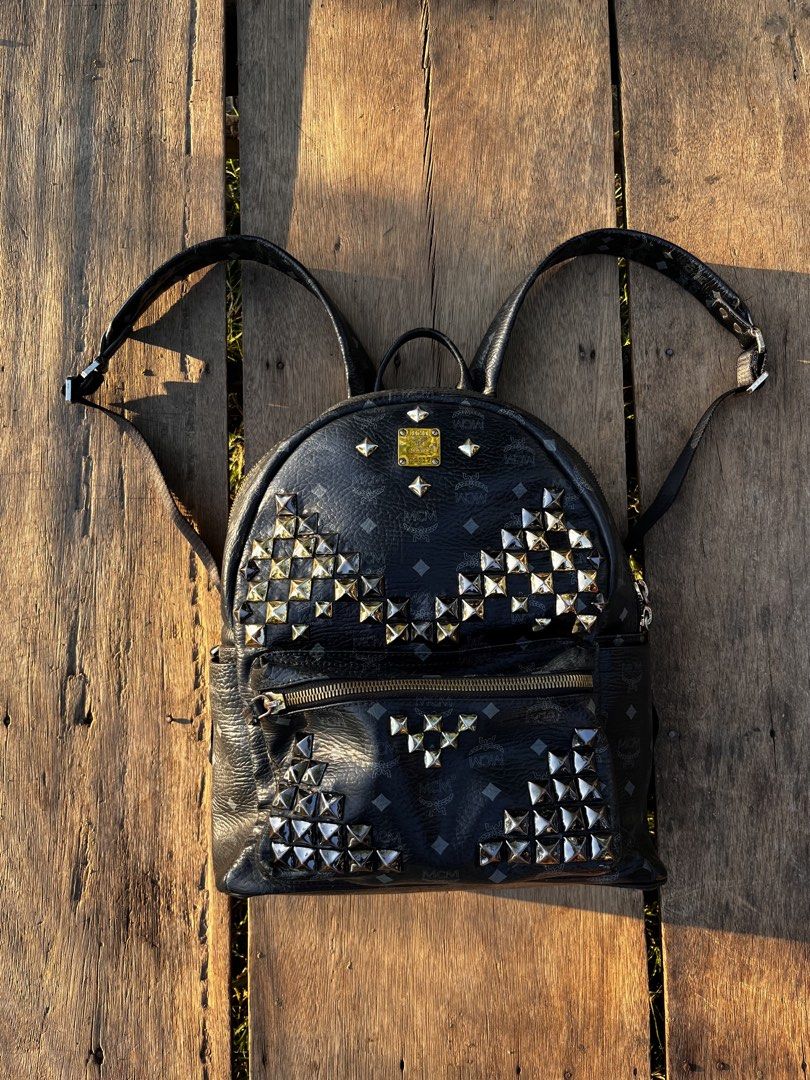 MCM Stark Studded Backpack Black Visetos Coated Canvas (Category: Backpacks) located in Mapandan. Submitted by thriftyfits.670 (Listing ID 1468927030, Image 1). Description: - Brand: MCM - Material: Visetos coated canvas in classic black with dark grey monogram - Hardware: Silver-tone and gold-tone metal pyramid studs, iconic brass logo plate - Pockets: Classic front zip pocket, two side slip pockets, and roomy interior - Straps: Top handle and a