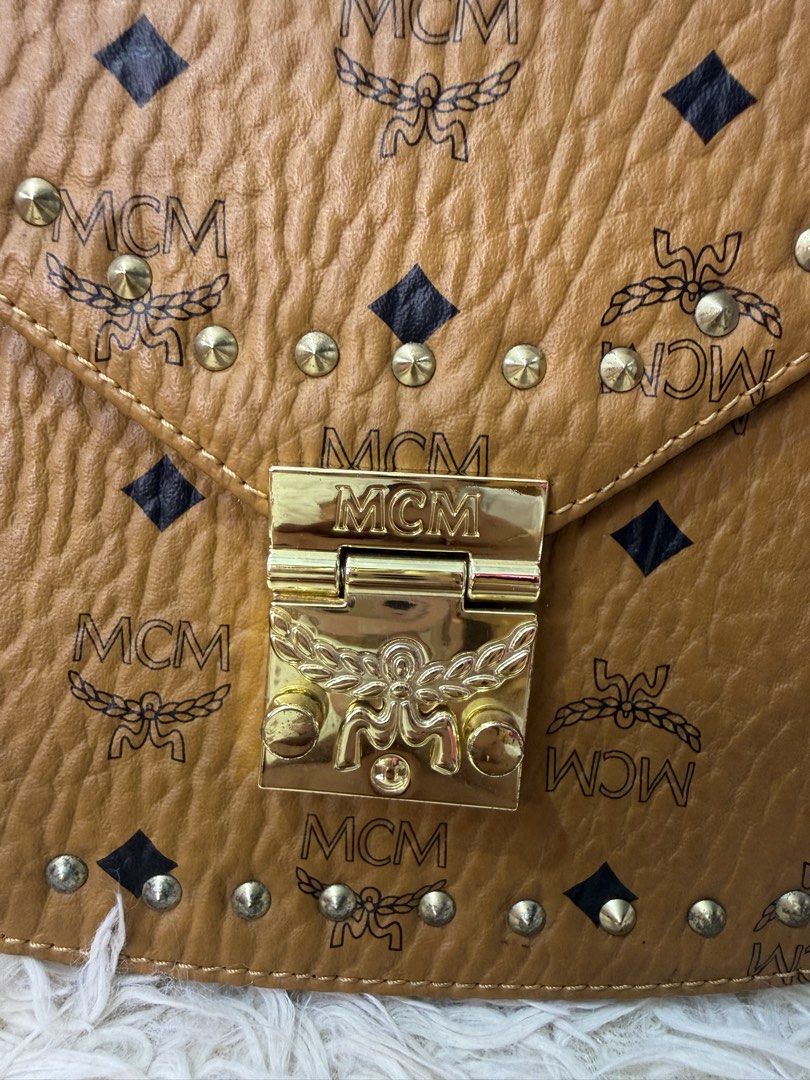 MCM Studded Crossbody Bag Cognac Monogram (Category: Luxury Bags & Wallets) located in Consolacion. Submitted by naome1. (Listing ID 1468876888, Image 2). Description: - Authentic quality MCM crossbody bag in timeless cognac - Signature monogram print with textured leather trim - Elegant gold-tone hardware and chic stud accents - Front flap closure featuring an engraved lock detail - Adjustable shoulder strap with unique H-shaped hardware links -