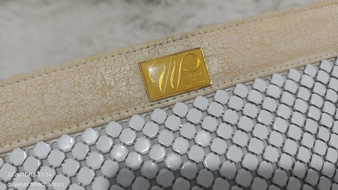 METAL MESH AUSTRALIA STYLE CLUTCH (Category: Clutches) located in Kalibo. Submitted by secondchances.thriftsh8p (Listing ID 1468890603, Image 3). Description: - Material: White mesh metal body with beige leather trim - Hardware & Details: Gold rectangular 'Symbol of Quality' brand badge and side zipper closure with leather pull tab - Interior: Clean beige fabric lining - Condition: Visible cracking and wear on the beige leather sections (priced a