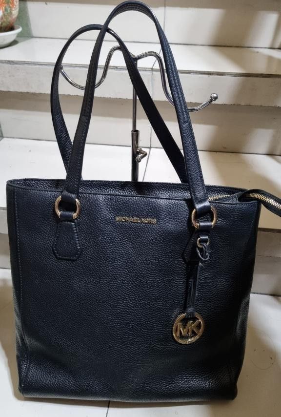 Michael kors leather tote bag (Category: Tote Bags) located in Manila. Submitted by onlinesmartshopping12 (Listing ID 1468781586, Image 2). Description: michael kors black - Stylish design - Made with durable leather. - Black Michael Kors tote bag. Features a zip closure, gold-tone hardware, and the MK logo. The bag has double handles and a textured leather exterior. The interior lining is black. The bag has a rectangular shape with a flat base. 