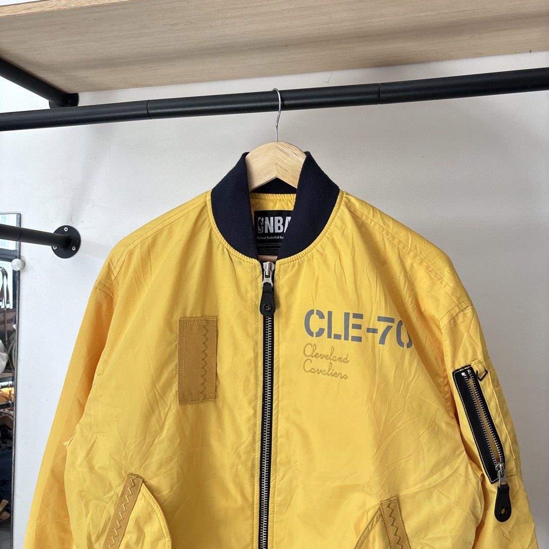 NBA Cleveland Cavaliers Yellow Bomber Jacket (Category: Coats, Jackets and Outerwear) located in Bambang. Submitted by heats777 (Listing ID 1468817872, Image 1). Description: - Official NBA Cleveland Cavaliers bomber jacket - Color: Vibrant yellow with dark blue ribbed collar, cuffs, and hem - Front design: 'CLE-70' and 'Cleveland Cavaliers' lettering - Back design: 'All For One, One For All' quote with inspirational boxed text - Pockets: Utility