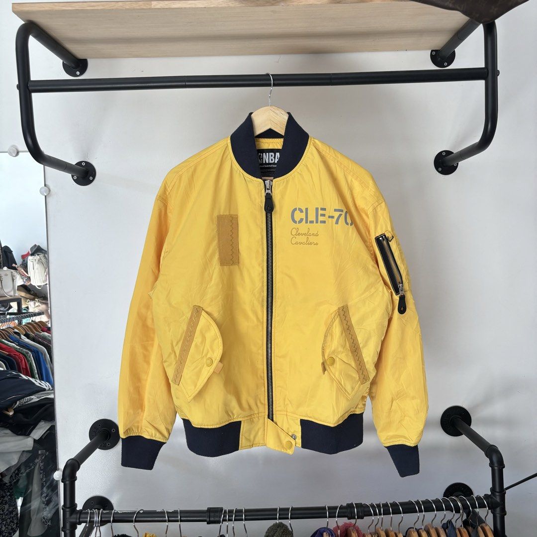 NBA Cleveland Cavaliers Yellow Bomber Jacket (Category: Coats, Jackets and Outerwear) located in Bambang. Submitted by heats777 (Listing ID 1468817872, Image 2). Description: - Official NBA Cleveland Cavaliers bomber jacket - Color: Vibrant yellow with dark blue ribbed collar, cuffs, and hem - Front design: 'CLE-70' and 'Cleveland Cavaliers' lettering - Back design: 'All For One, One For All' quote with inspirational boxed text - Pockets: Utility