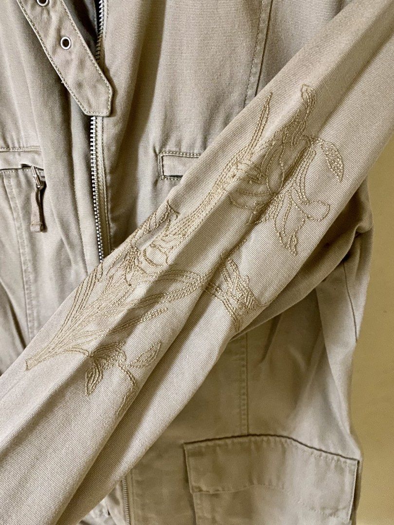 NEXT Khaki Utility Jacket Size UK 12 EUR 40 (Category: Coats, Jackets and Outerwear) located in Baguio. Submitted by vintagefox (Listing ID 1468808944, Image 2). Description: - Brand: NEXT - Size: UK 12 / EUR 40 - Color: Khaki - Material: Sturdy cotton canvas - Closure: Full zip with buckled high collar and metal eyelets - Pockets: Multiple front pockets with zippers and flaps - Detail: Subtle tonal floral embroidery on the left sleeve.