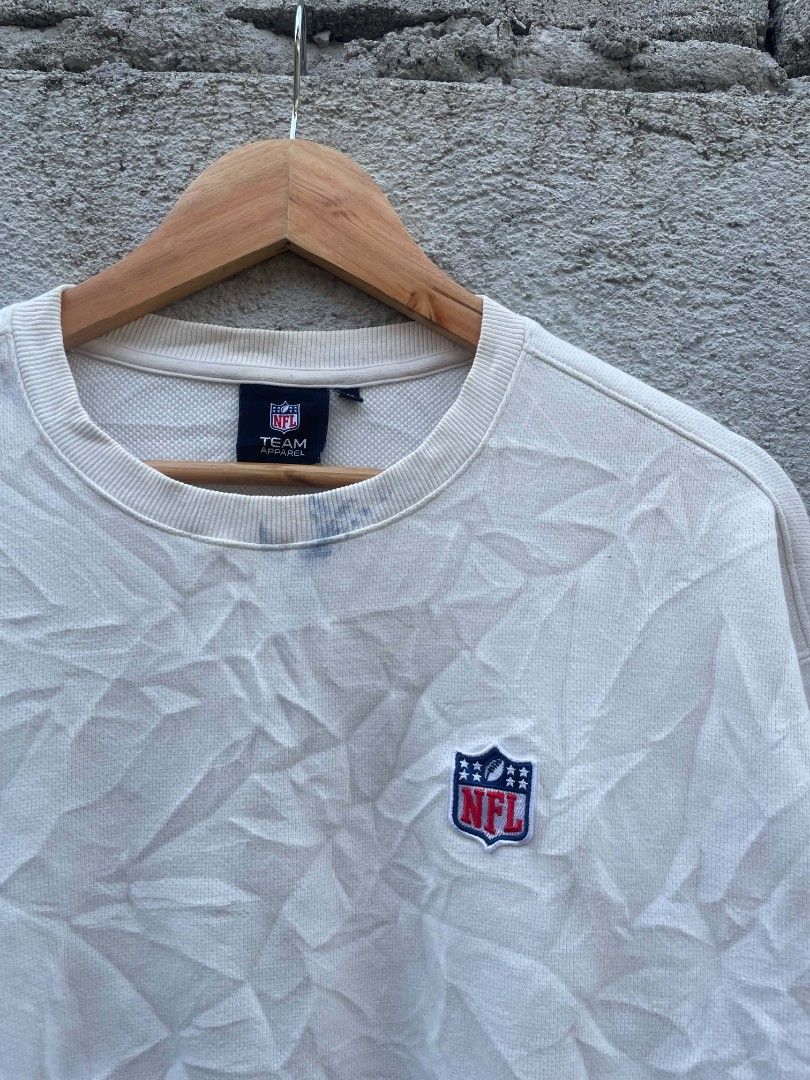 NFL Team Apparel White Crewneck Sweatshirt Medium (Category: Coats, Jackets and Outerwear) located in Banga. Submitted by its.zayn11e (Listing ID 1468713068, Image 3). Description: - Brand/Style: NFL Team Apparel off-white crewneck sweatshirt - Size: Medium - Design: Large NFL shield graphic on the back, small front chest logo, and woven tag near the bottom hem - Details: Classic ribbed cuffs, collar, and hem - Perfect for casual streetwear and g