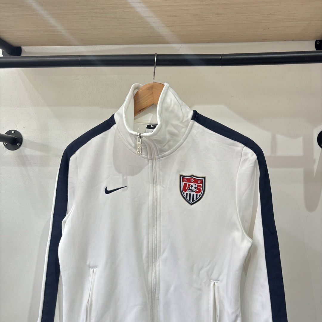 Nike US Soccer Track Jacket White Navy (Category: Coats, Jackets and Outerwear) located in Bambang. Submitted by heats777 (Listing ID 1468827914, Image 1). Description: - Brand: Nike (Official US Soccer merchandise) - Color: White with navy stripes - Size: Medium - Material: 53% polyester, 47% cotton (Body); 99% polyester, 1% spandex (Ribbing) - Design: Embroidered US Soccer crest on front, bold USA lettering on back - Features: Full zip closure,