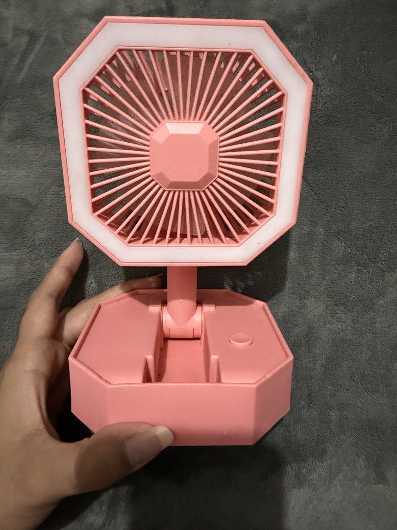 Pink portable folding desk fan with LED ring light (Category: Fans) located in Mandaluyong City. Submitted by josa_xox0i8 (Listing ID 1468747405, Image 2). Description: Compact and foldable mini desk fan with a built-in LED ring light. Great for personal cooling, makeup/selfie lighting, study tables, or bedside nightstands. Design: Octagonal frame, foldable base for easy storage and portability Features: Built-in LED light ring, rechargeable via 