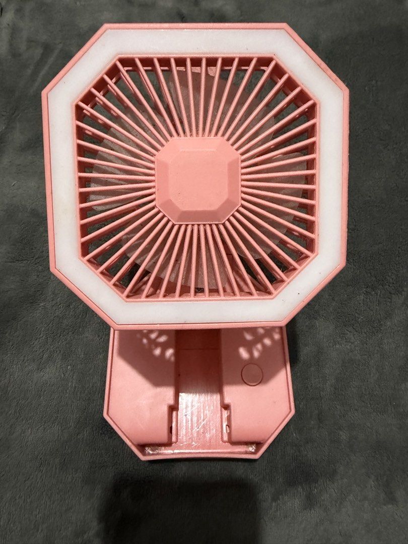 Pink portable folding desk fan with LED ring light (Category: Fans) located in Mandaluyong City. Submitted by josa_xox0i8 (Listing ID 1468747405, Image 1). Description: Compact and foldable mini desk fan with a built-in LED ring light. Great for personal cooling, makeup/selfie lighting, study tables, or bedside nightstands. Design: Octagonal frame, foldable base for easy storage and portability Features: Built-in LED light ring, rechargeable via 